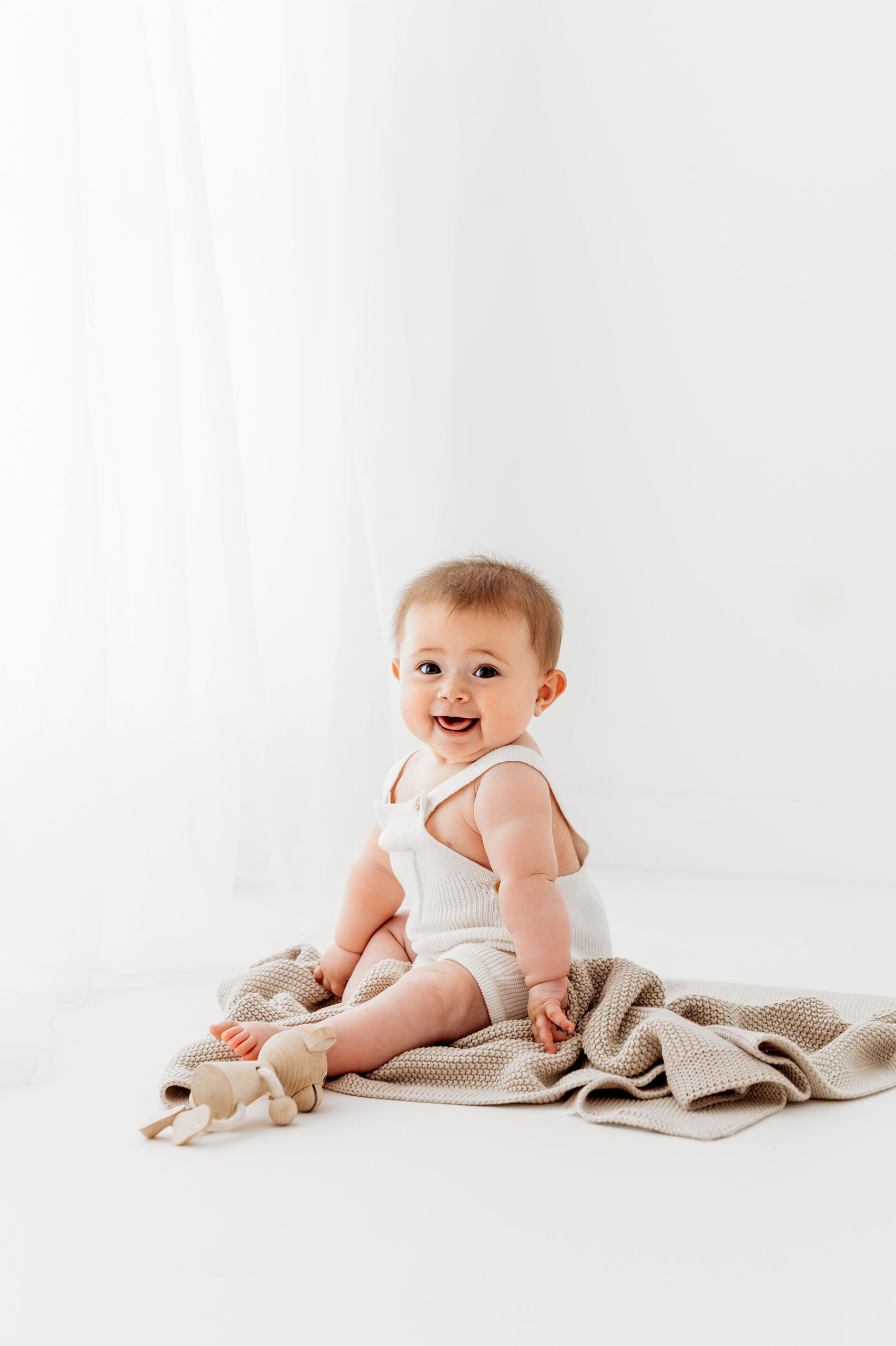 Baby photoshoot- baby girl sitting on beige blanket in a white romper