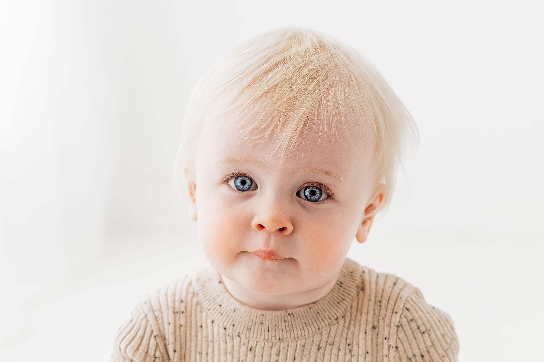 Baby girl wearing beige romper, looking directly at the camera