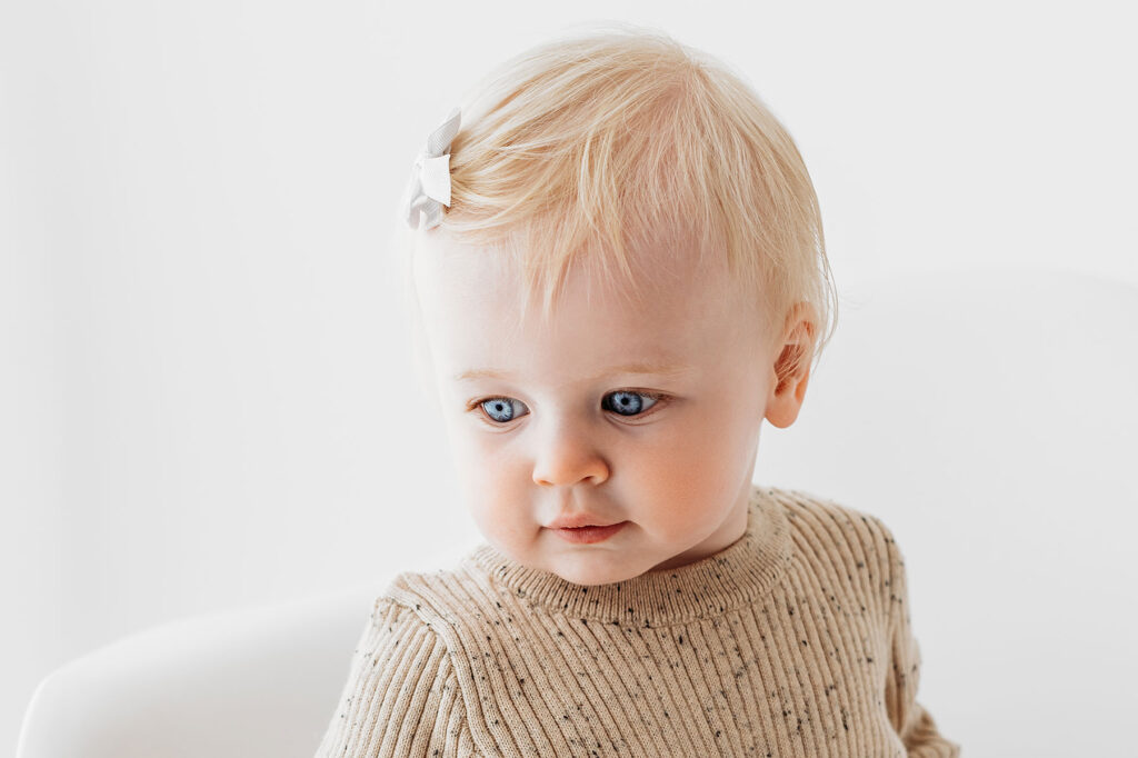 Baby girl wearing beige romper, and white bow in her hair