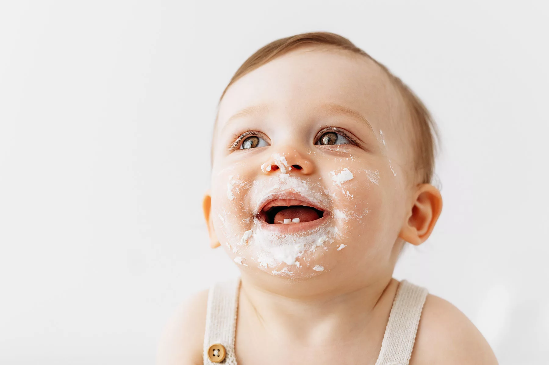 Baby boy smiling with big brown eyes and cake around his mouth. Sidcup cake smash photoshoot.