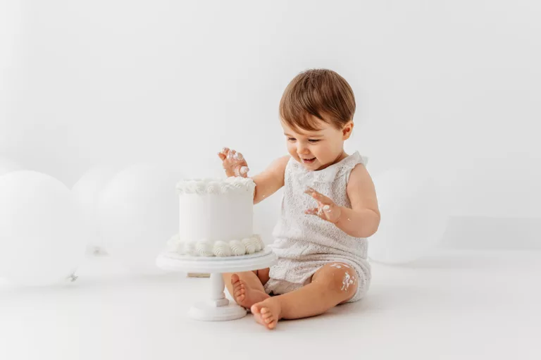 Sidcup cake smash photographer- baby sitting touching white cake
